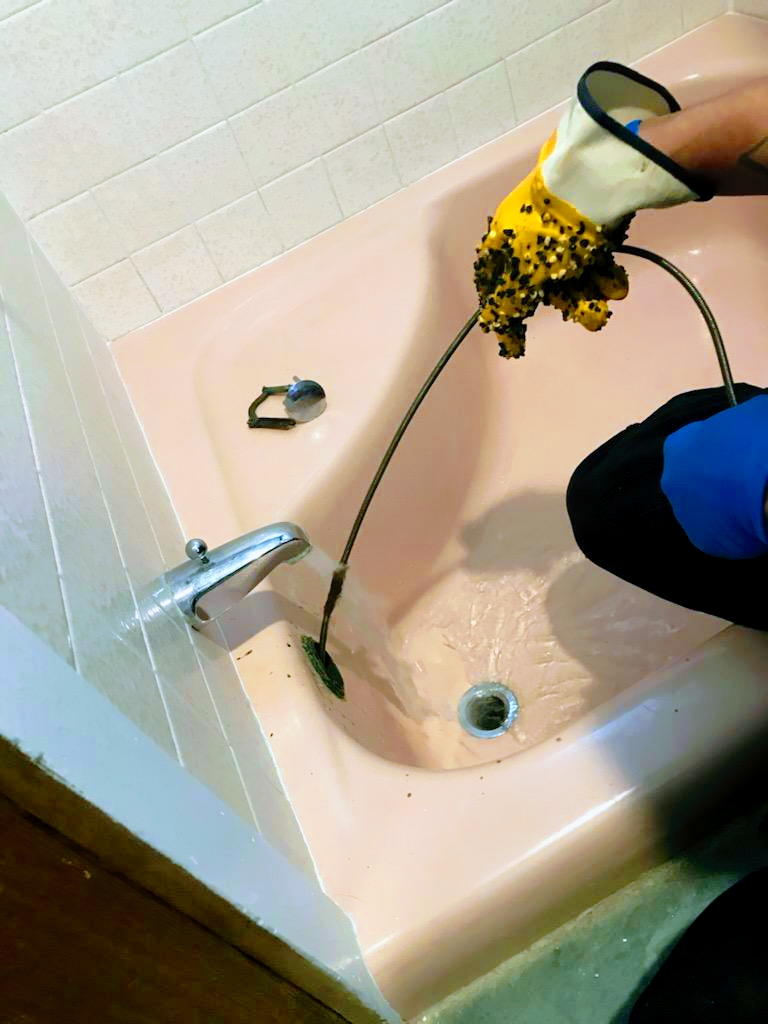 Gloved hand feeding a drain cable into a bathtub drain