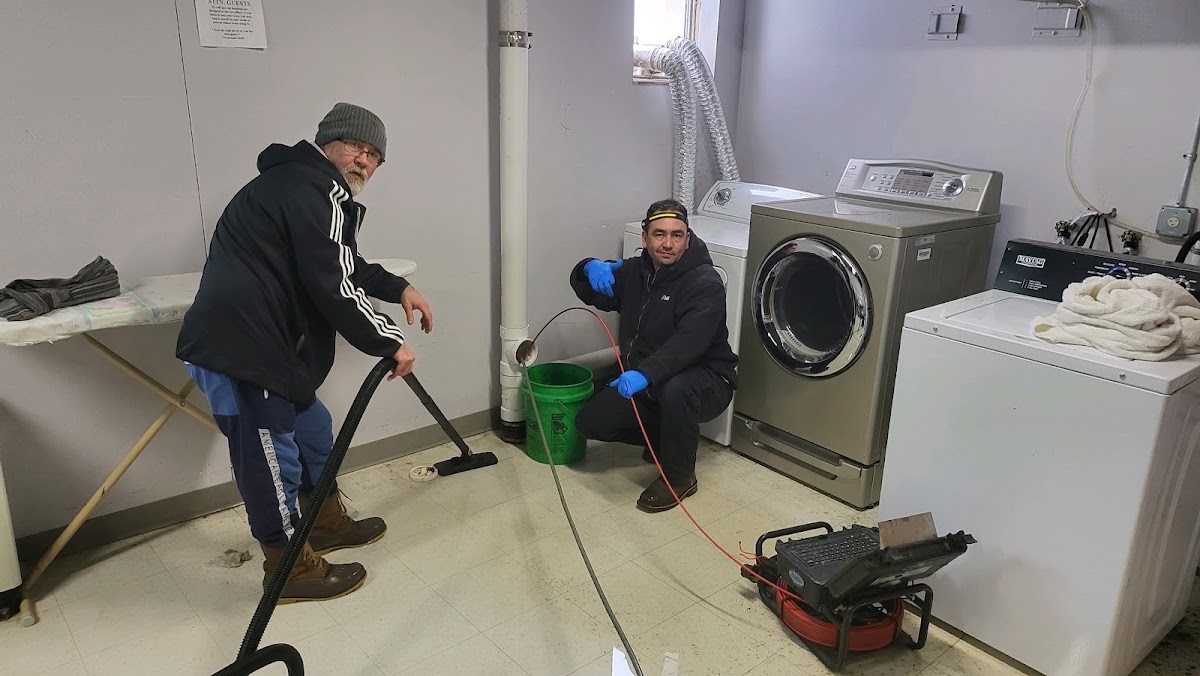 Two technicians working in a laundromat back room with a drain machine