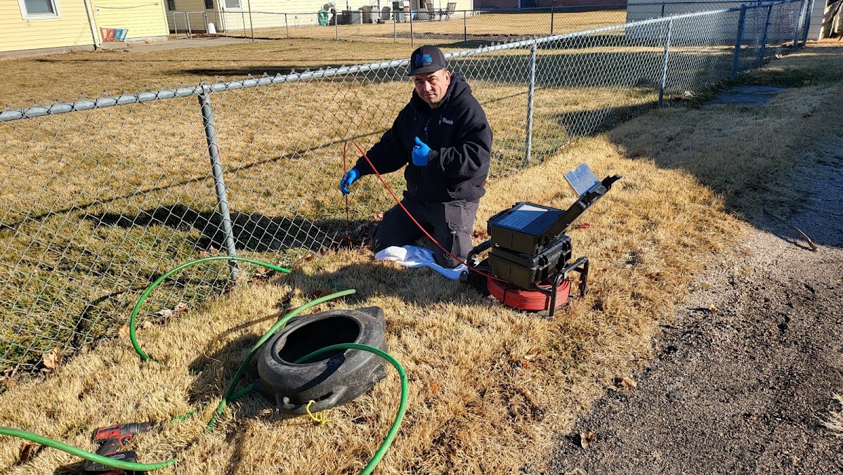 Technician kneeling at a yard cleanout with a sewer camera rig